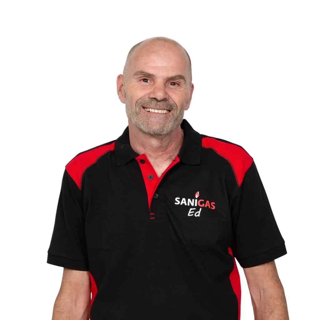 Veiligheidsmedewerker in zwart-rood werkshirt met Sanigas-logo, lachend tegen witte achtergrond.