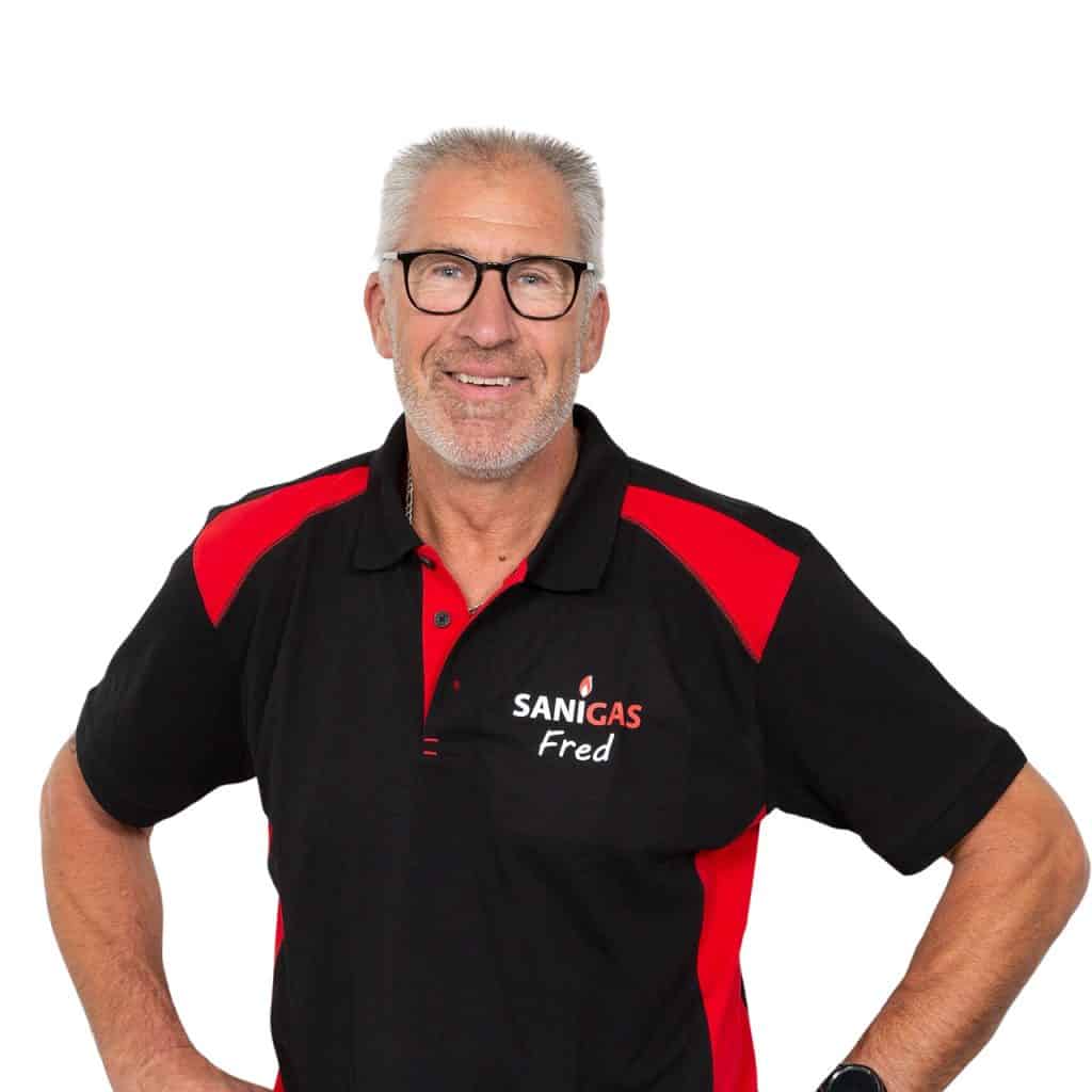 Professionele man in Sanigas uniform, specialist in gas- en verwarmingsinstallaties, lachend met wit haar en bril, poseert met hand aan de heup, vakbekwaam en betrouwbaar.