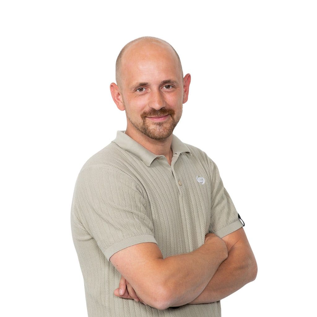 Biervriendelijk man met korte baard en gespannen armen, gekleed in een beige polo, favoriet voor zakelijke en professionele portretfoto's, representatief en vriendelijk.