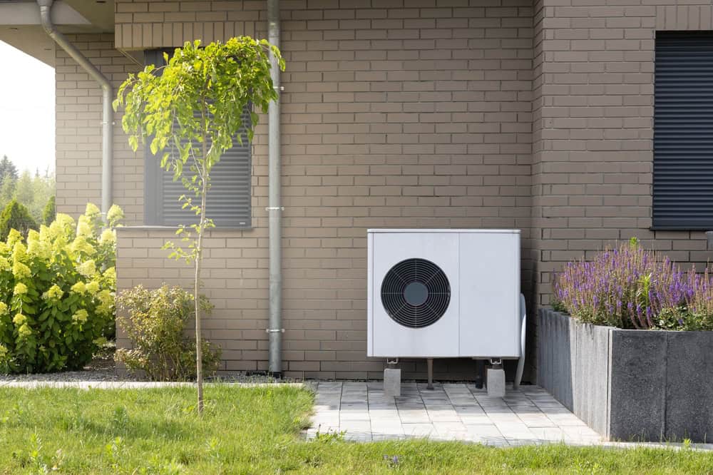 Warmtepomp buitenunit geïnstalleerd naast een woning met tuin, een duurzame oplossing voor energiebeheer en verwarming, passend bij de diensten van Sanigas voor milieuvriendelijke installaties.